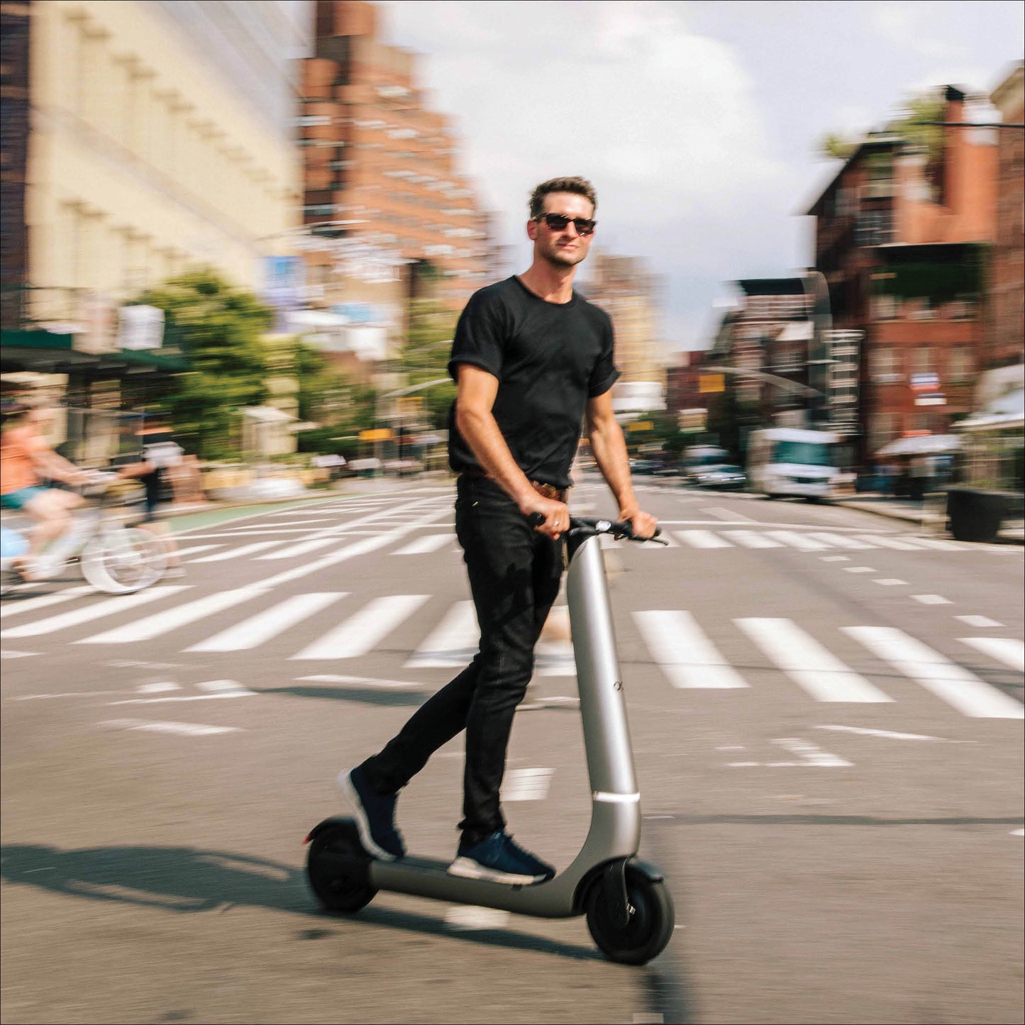 Man riding a electric scooter on a city street with buildings and pedestrians in the background
