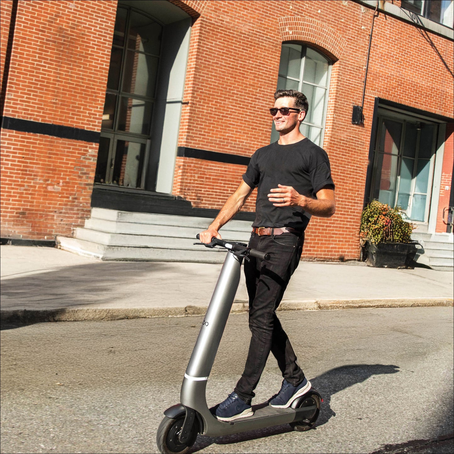 Man riding a scooter on a street with a brick building in the background