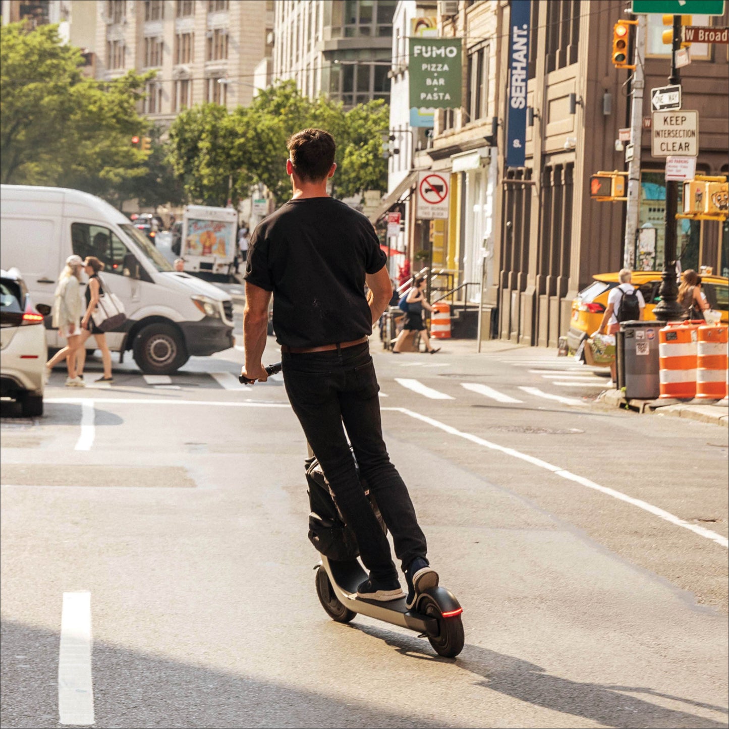 Person riding an electric scooter on a city street with buildings and traffic in the background