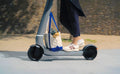 Person riding a scooter with a bag attached on a sidewalk