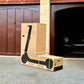 Box with a scooter on the ground in front of a garage