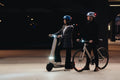 Two people with electric scooters and bicycles at night.