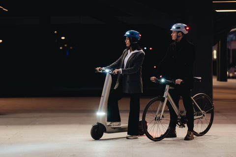 Two people with electric scooters and bicycles at night.
