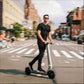 Man riding a electric scooter on a city street with buildings and pedestrians in the background