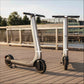 Two electric scooters on a wooden deck with a bridge and trees in the background.