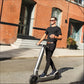 Man riding a scooter on a street with a brick building in the background