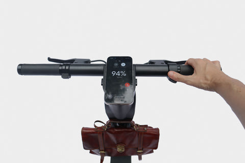 Hand holding a scooter handlebar with a smartphone displaying battery percentage on a white background