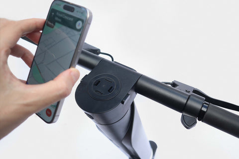 Hand holding a smartphone next to an electric scooter with a phone mount.